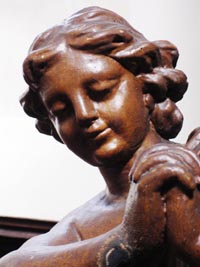 Un ange adorateur particulièrement recueilli nous apparaît les mains jointes. Sculpté dans un bois tendre et peint en brun moyen, il est de belle facture. Les yeux mi-clos, il nous entraîne dans une méditation profonde. Il possède son pendant de l’autre côté de l’autel.